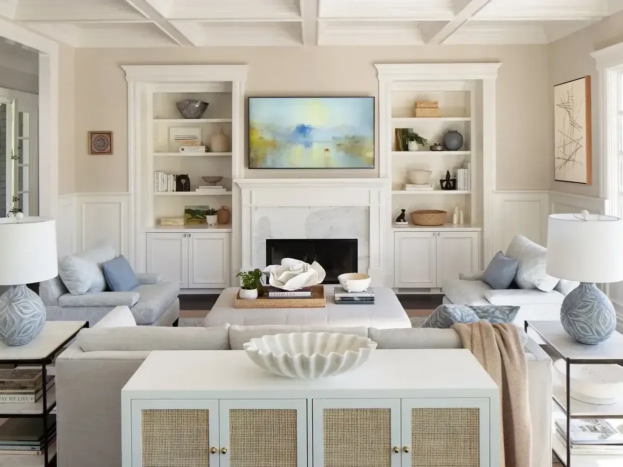 A bright and cozy coastal-inspired living room featuring a white sofa, built-in bookshelves, and a woven console table.