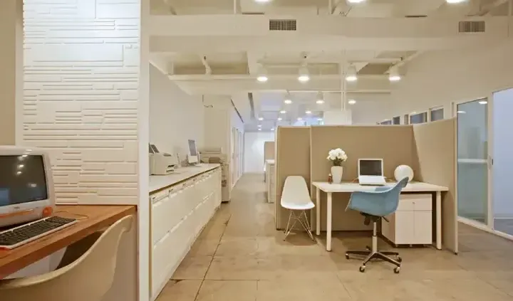 A modern and bright office interior in Singapore with white desks, light wood flooring, and beige privacy partitions.