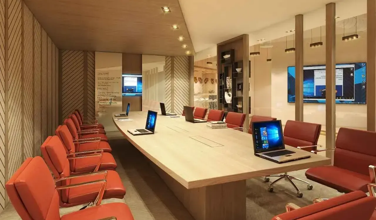 A bright and spacious modern conference room with a long table, orange chairs, and dual display screens for presentations.