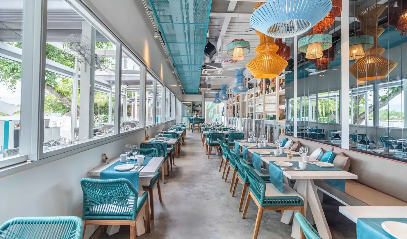 A bright and modern restaurant interior in Singapore with rows of tables, turquoise chairs, and a vibrant color palette.