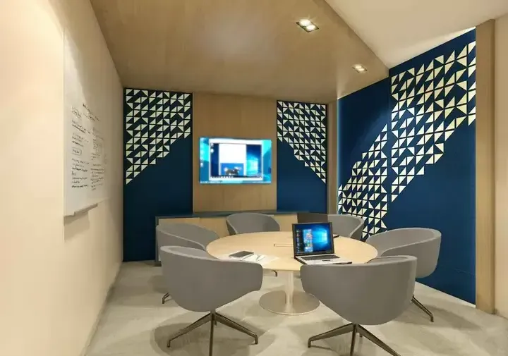 A modern corporate meeting room with bold blue accent walls, a round table, and a wall-mounted screen for presentations.
