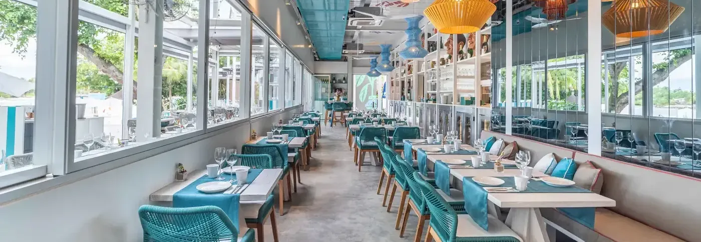 A bright and modern restaurant interior in Singapore with rows of tables, turquoise chairs, and a vibrant color palette.